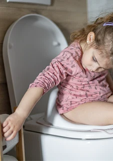 Ett barn sitter på en potta och sträcker sig efter toalettpapper. 