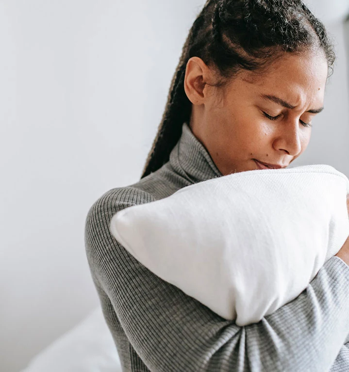 En kvinna ser bekymrad ut och kramar om en kudde. 