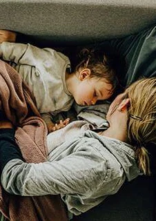 En mamma som sover tillsammans med sitt febriga barn i soffan.