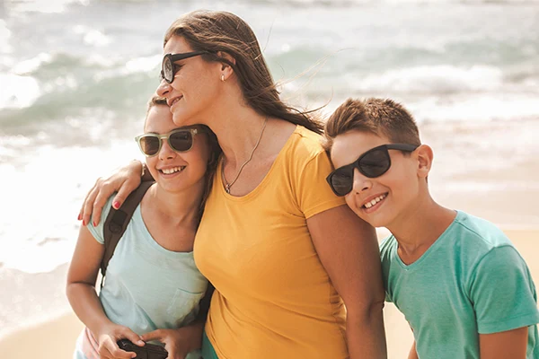 En mamma kramar om sina två barn på stranden. 