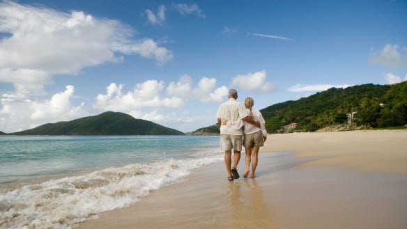 Ett äldre par promenerar på en sandstrand.