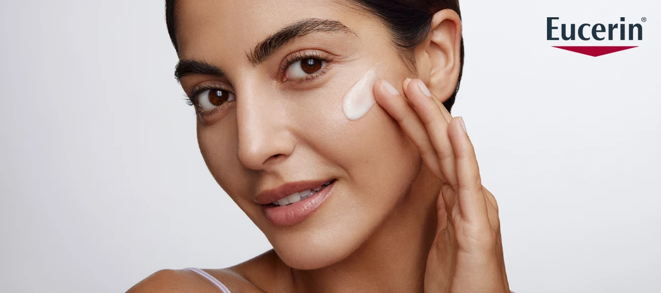 Kvinna applicerar ansiktskräm; Eucerin-logotyp i hörnet.