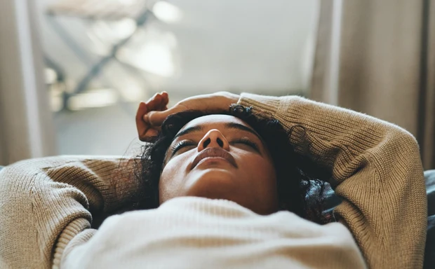 En kvinna ligger i en säng med händerna ovanför huvudet. 